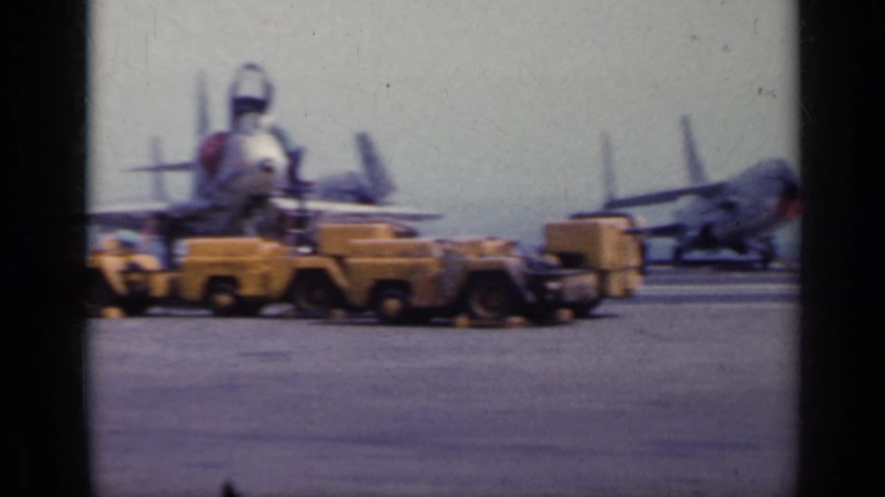 Aircraft nose facing camera with yellow ground vehicles crossing the tarmac.
