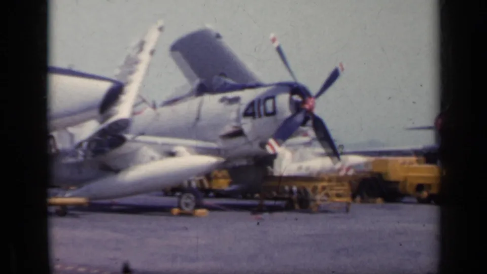 1962 Italy 8mm frame showing parked U.S. Navy aircraft marked 410 with open panels and ground equipment on a deck area.