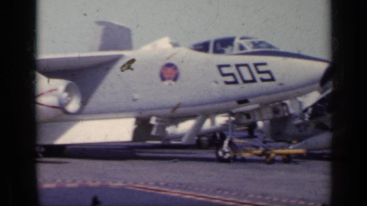 Gray Navy jet marked 505 parked beside deck equipment and a small cart.
