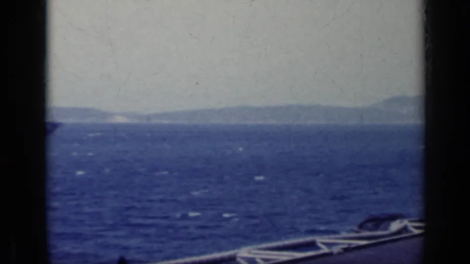 1962 Italy 8mm frame looking across blue open water toward a low, distant coastline from a ship or dock edge.