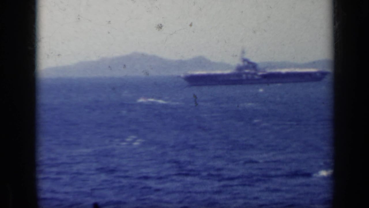 Naval ship on blue sea with distant mountains and hazy sky.