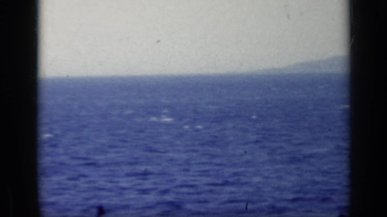 1962 Italy seascape frame with open water, pale sky, distant landform, and visible 8mm frame borders.
