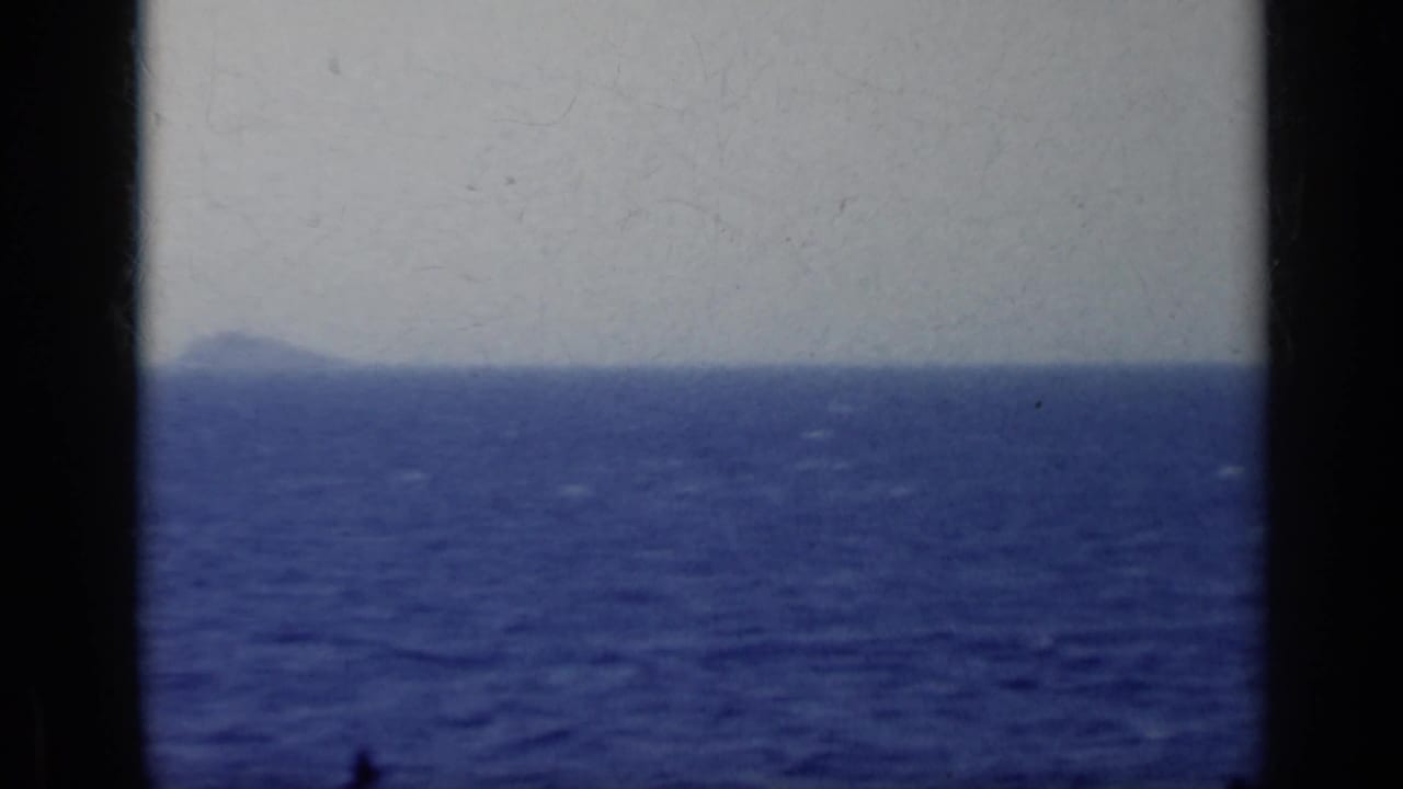 Hazy coastline or island across blue open water, seen through dark film-frame edges.