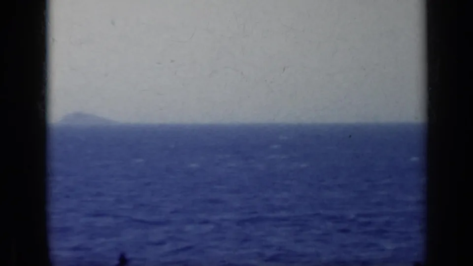 1962 8mm shipboard view of blue sea and a distant hazy landform, with no people visible.