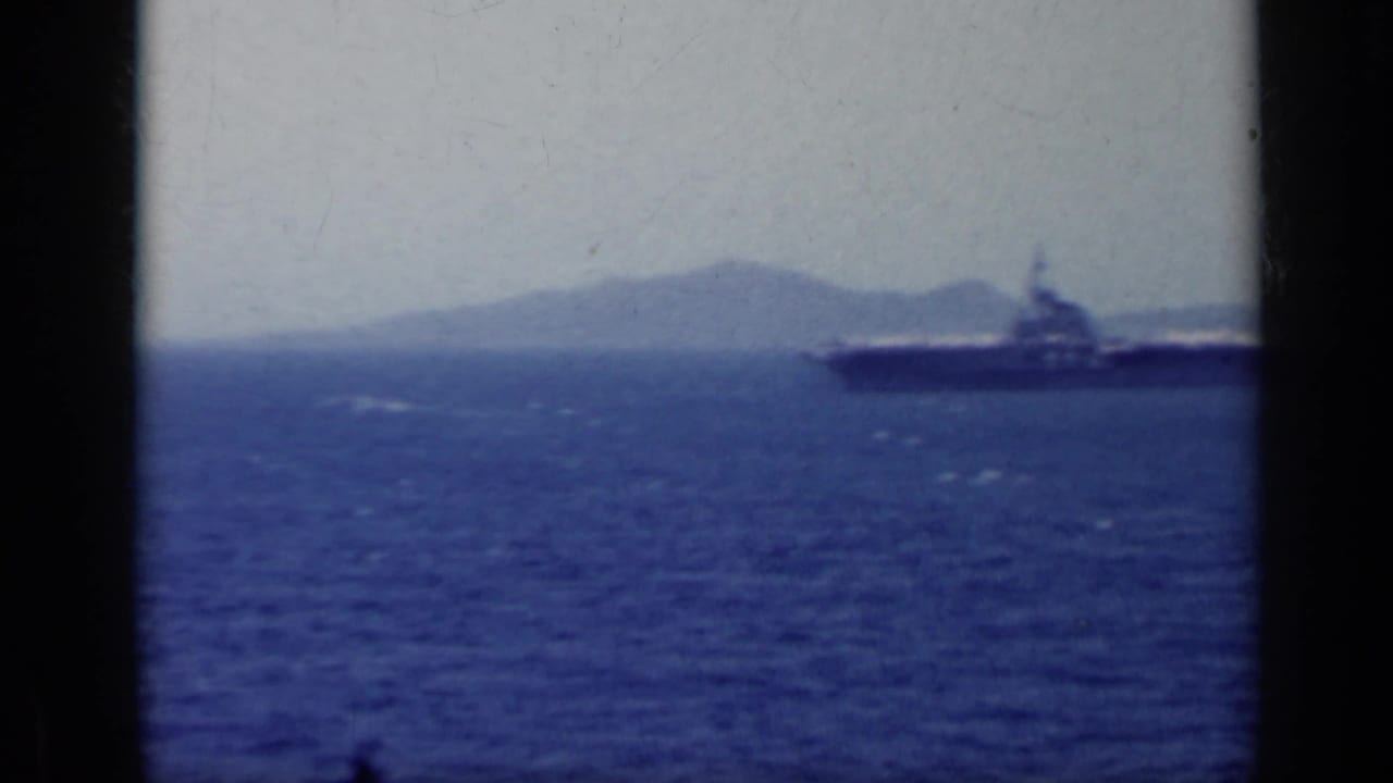 Large naval vessel on blue water with a hazy landform behind it.