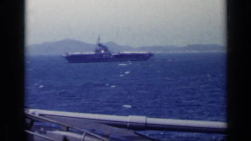 1962 8mm shipboard angle showing a naval vessel across the water, with deck rail in the foreground.