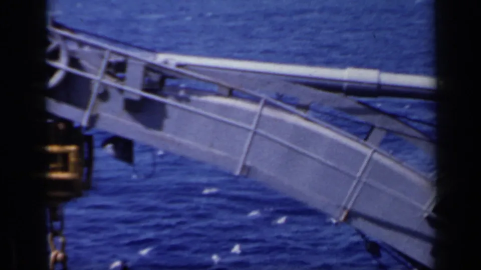 1962 8mm close shipboard view of crane-like rigging and railings above deep blue water.