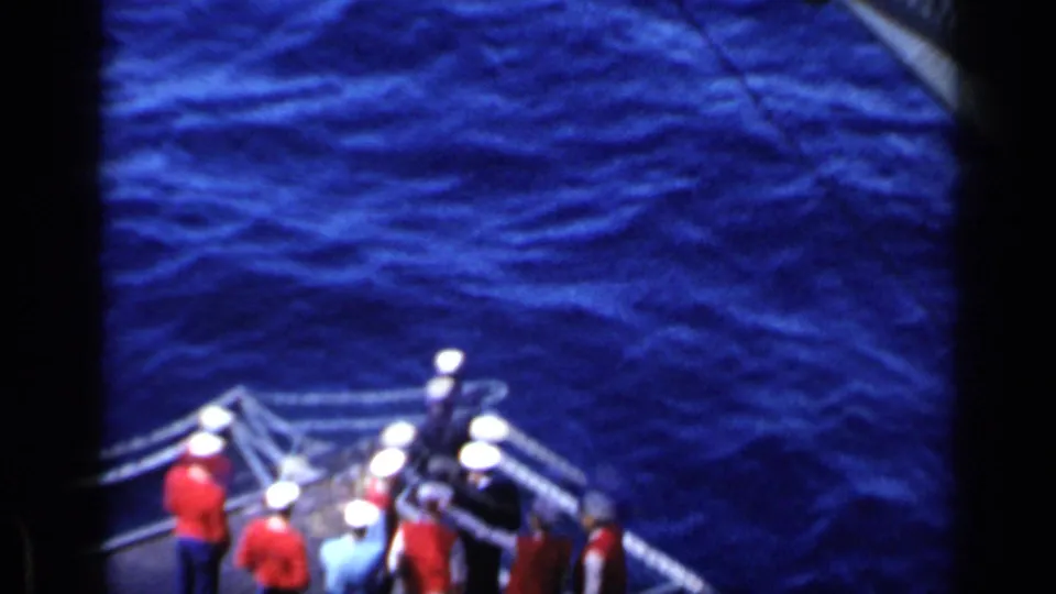 1962 Italy home-movie frame showing aircraft-carrier crew gathered at the deck edge with open sea filling the background.