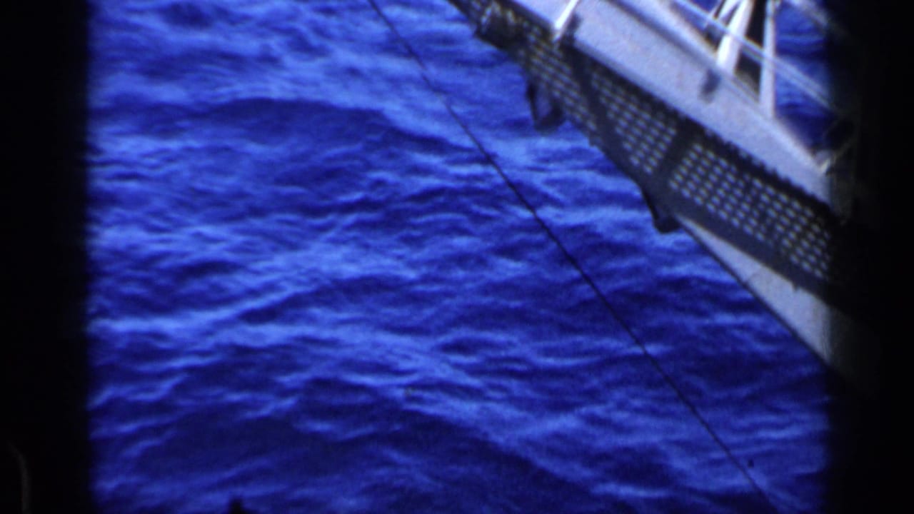 Blue ocean seen through dark frame bars with part of a metal vessel structure overhead.