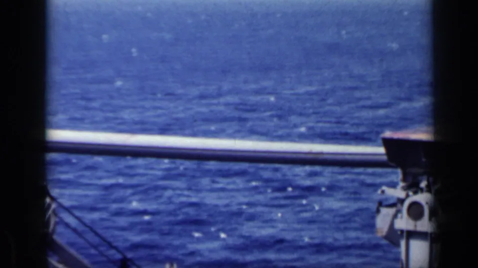 1962 Italy 8mm view from a boat or rig, with blue water, a horizontal rail, and dark frame bars in the foreground.