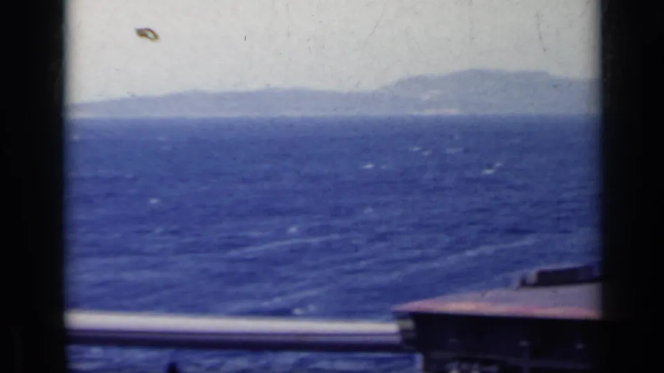 1962 Italy 8mm frame showing a distant landmass across the sea, with boat railings and dark foreground framing.