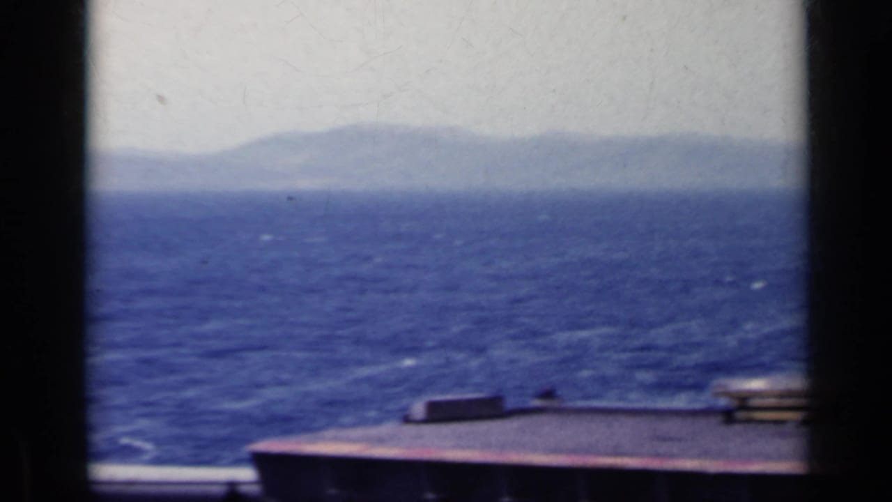 1962 Italy 8mm frame showing blue water, a distant hazy shore, and part of the filming vessel in the foreground.