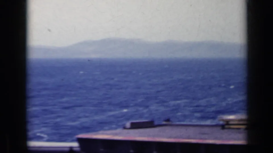 1962 Italy 8mm frame showing blue water, a distant hazy shore, and part of the filming vessel in the foreground.