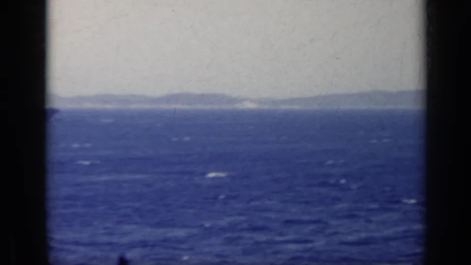 1962 Italy 8mm view of blue open water and distant mountainous coastline seen through dark window-like framing.