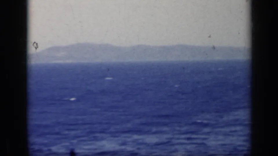 Italy 1962 8mm travel view of distant mountains across open water, with soft color and visible film texture.
