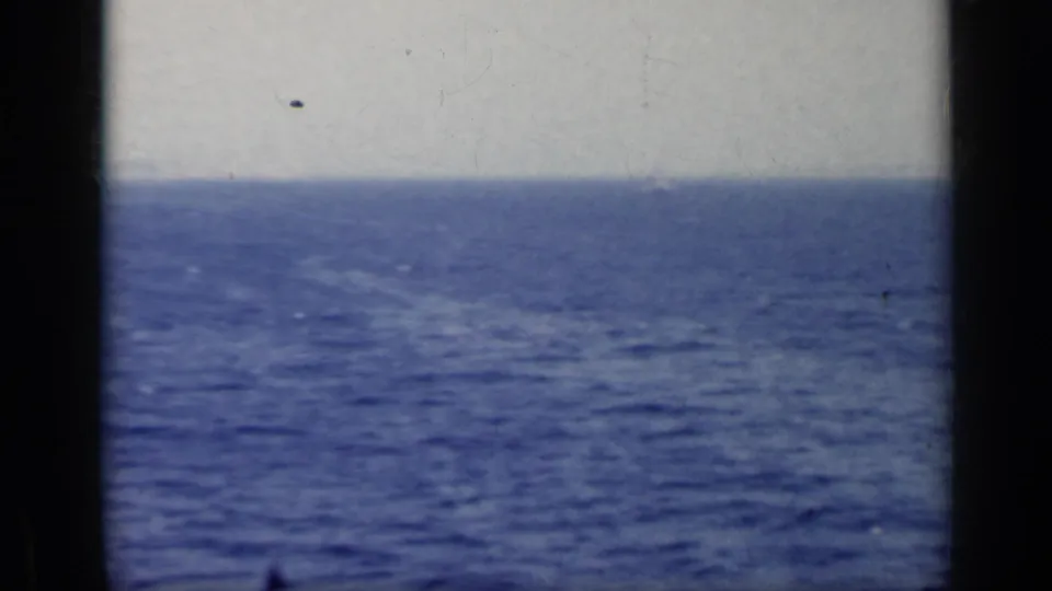 1962 Italy 8mm frame with rippled blue sea, overcast sky, horizon, and dark foreground bars dividing the view.