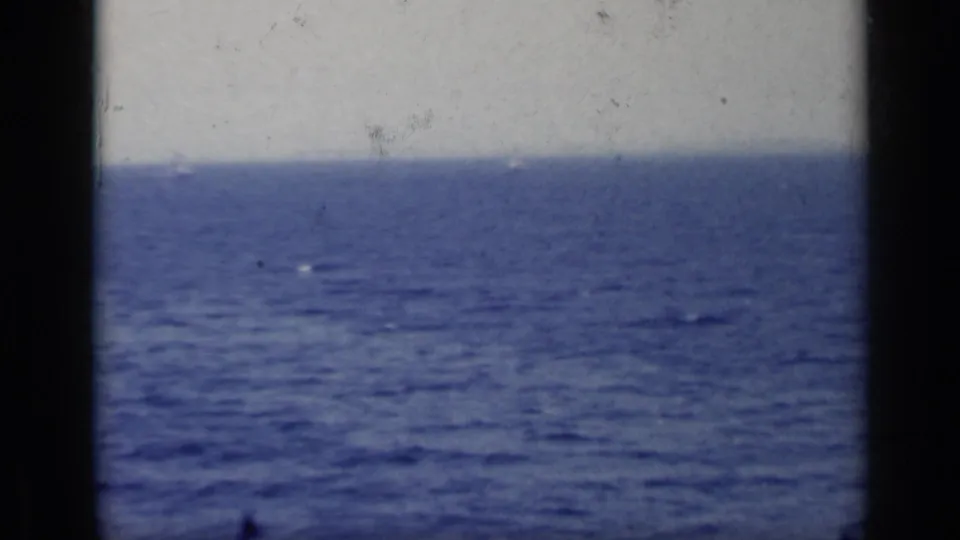 Vintage 8mm Italy frame showing a soft blue sea horizon through a dark window or railing frame, with no people visible.