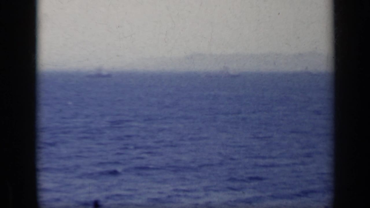 Blue sea and pale sky divided by a hazy horizon, framed by dark film borders.