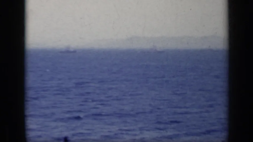 1962 Italy 8mm frame showing open blue sea, pale sky, and distant landforms through dark film gate edges.