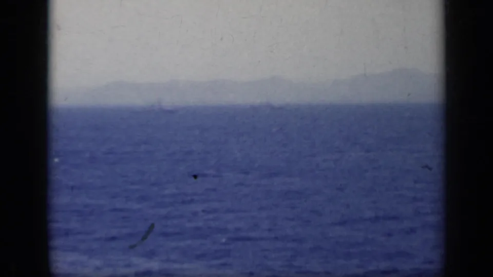 1962 Italy coastal view on 8mm film, with blue water, pale sky, and distant shoreline barely visible on the horizon.