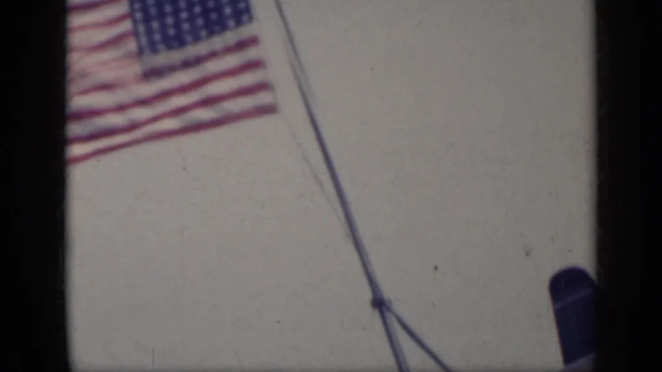 American flag fluttering on a ship at sea in 1962 8mm footage, with rigging and ocean visible.
