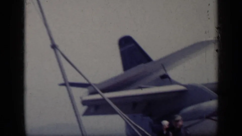 Large aircraft tail, wing, and deck structure on a U.S. carrier in 1962 home-movie footage near Italy.