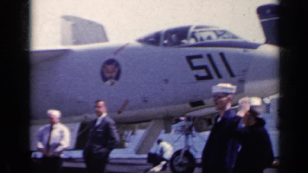 Sailors stand on an aircraft carrier deck beside a U.S. Navy jet marked 511.