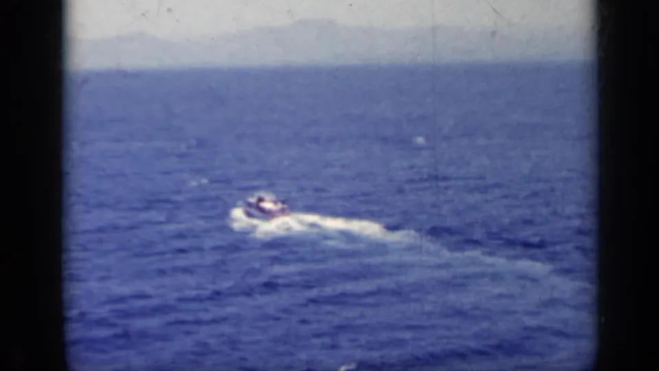 A small motorboat crosses deep blue water in 1962 Italy-linked home-movie footage from a naval setting.