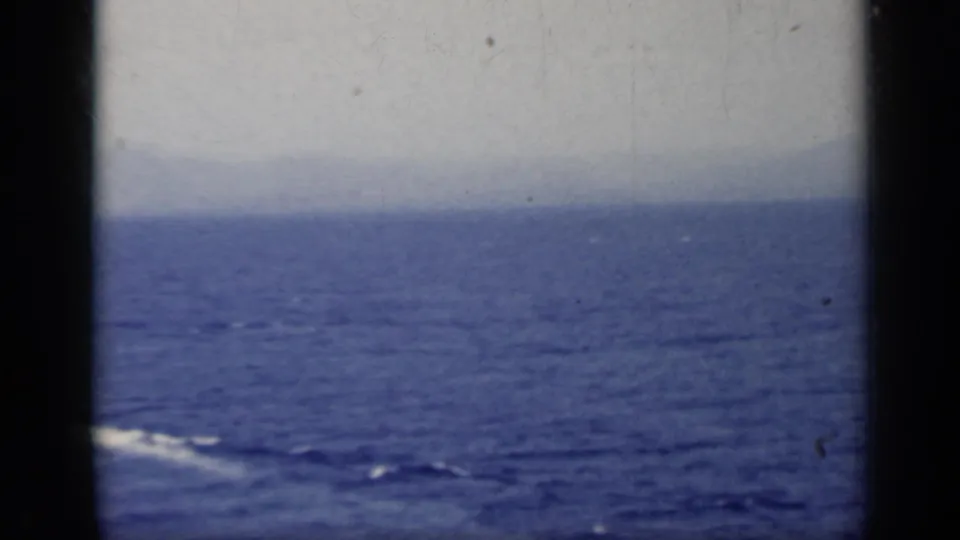 A mostly open-sea view shows faint boat wake, distant haze, and the soft blue cast of 8mm footage.