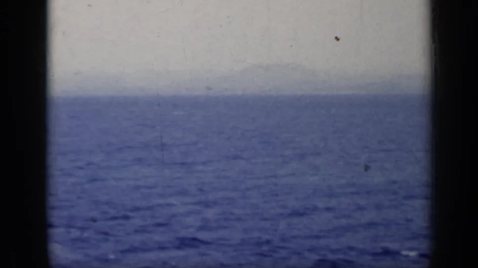 1962 Italy home-movie frame showing open blue lake water, a pale sky, and a faint distant shoreline viewed from a moving vessel.