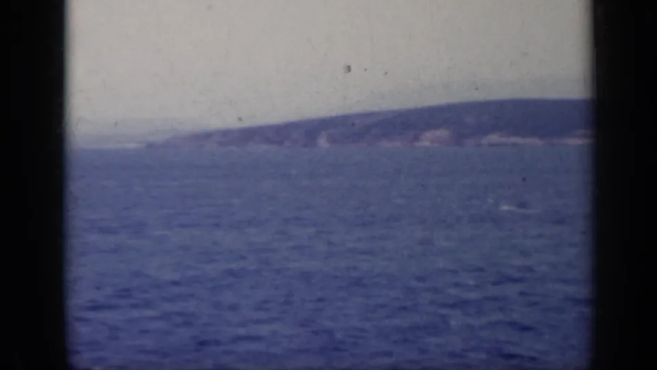 1962 Italy lake view with rippled blue water, low distant hills, and soft film grain across the frame.
