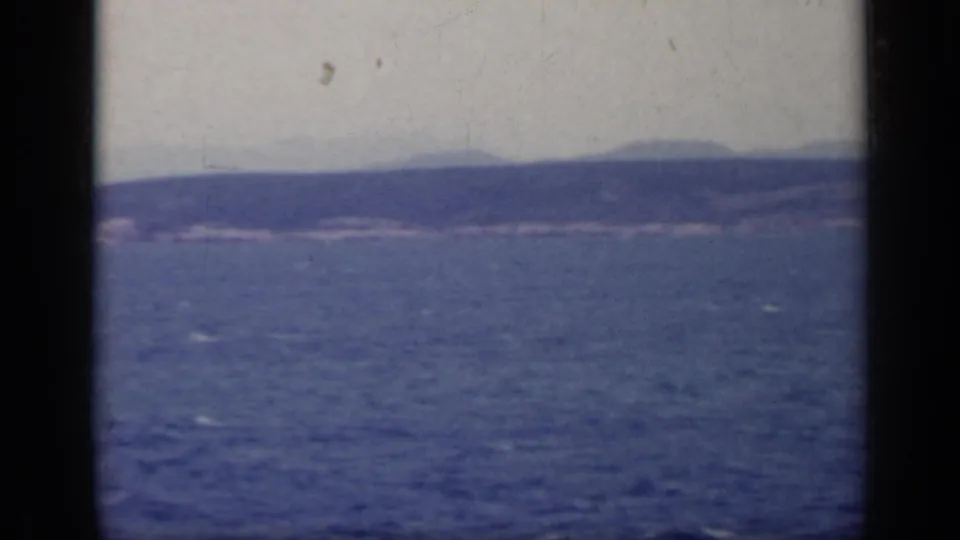 1962 Italy home-movie view of lake water, low shoreline, and hazy hills, with visible grain and dust from the film scan.