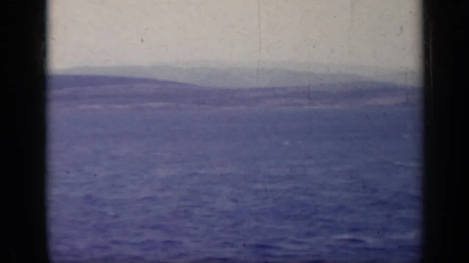1962 Italy lake panorama with blue water, a distant hillside, pale sky, and visible 8mm film wear.