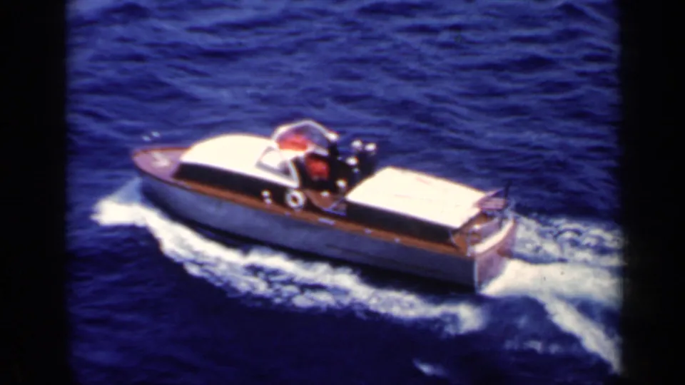 A small speedboat with wooden trim and a white canopy cuts through blue water in 1962 Italy home-movie footage.