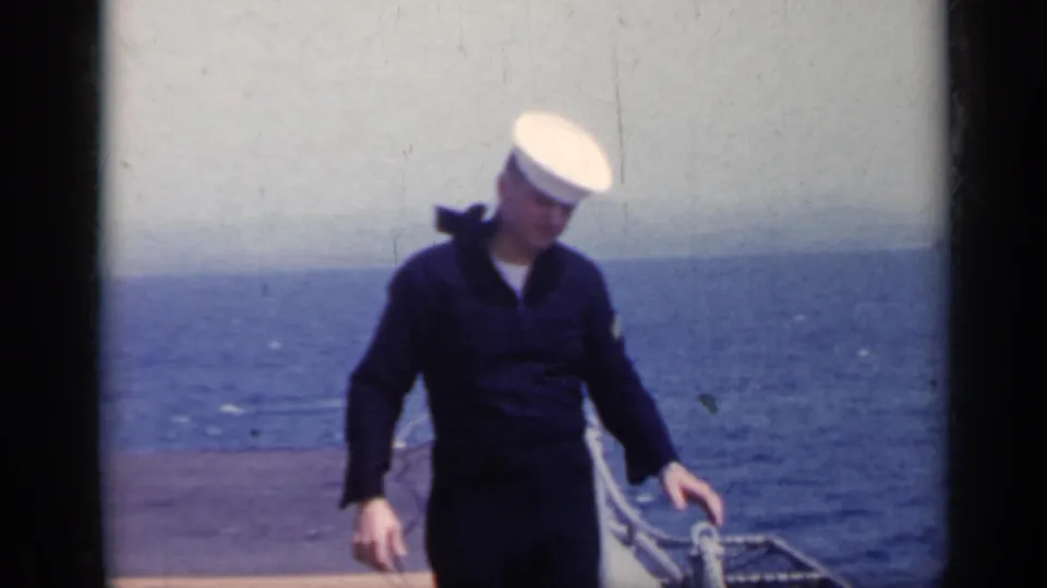 A young sailor in a dark uniform and white cap stands on a pier beside the sea in 1962 Italy archival home-movie footage.