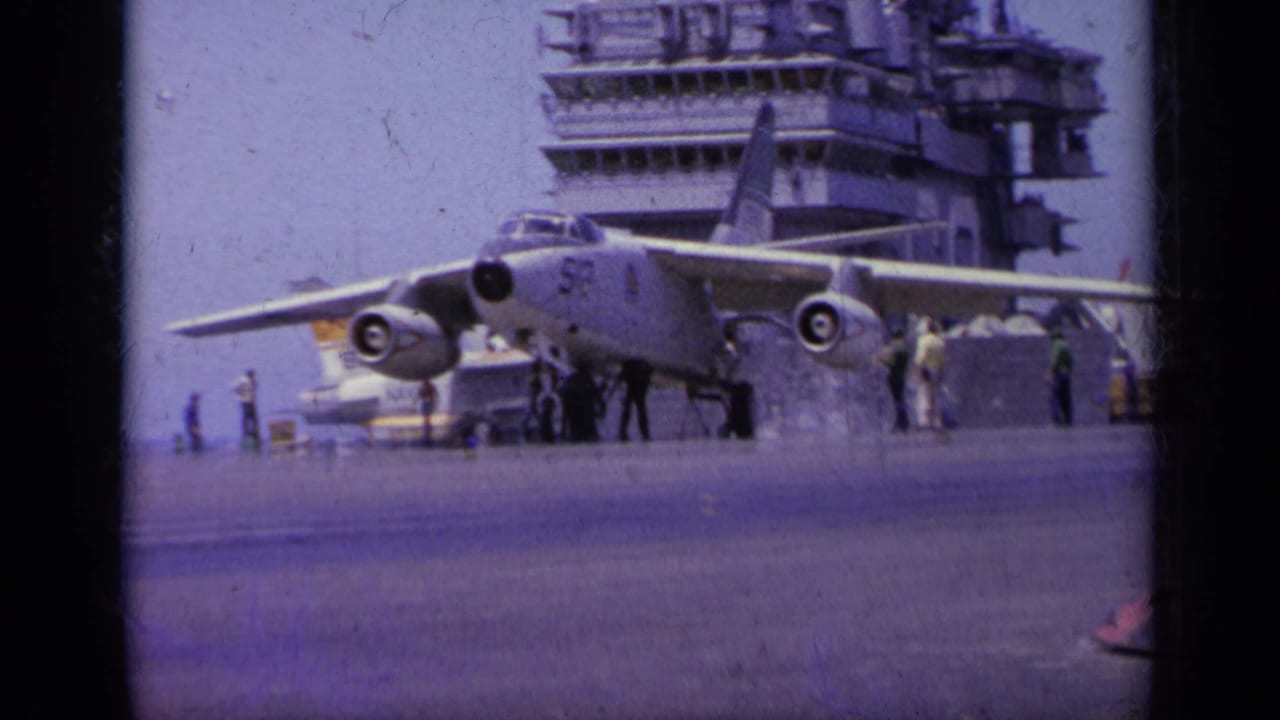 Jet aircraft parked or taxiing on an aircraft carrier deck with the ship island behind it.