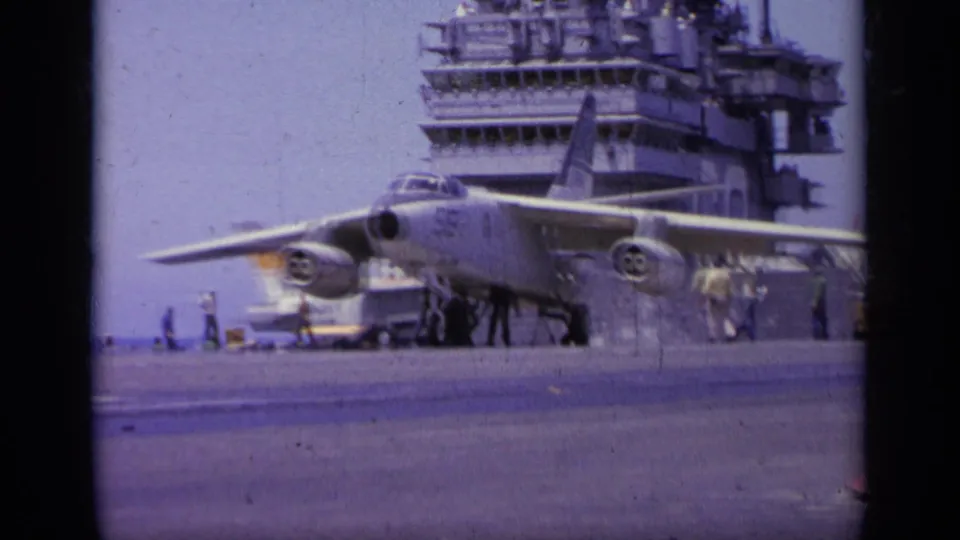 A 1963 carrier-deck view in Greece shows a Navy jet aligned on deck while crew members stand near the aircraft and island.