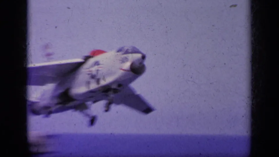 1963 Greece 8mm frame showing a jet aircraft just after launch from an aircraft carrier deck, with ocean behind it.