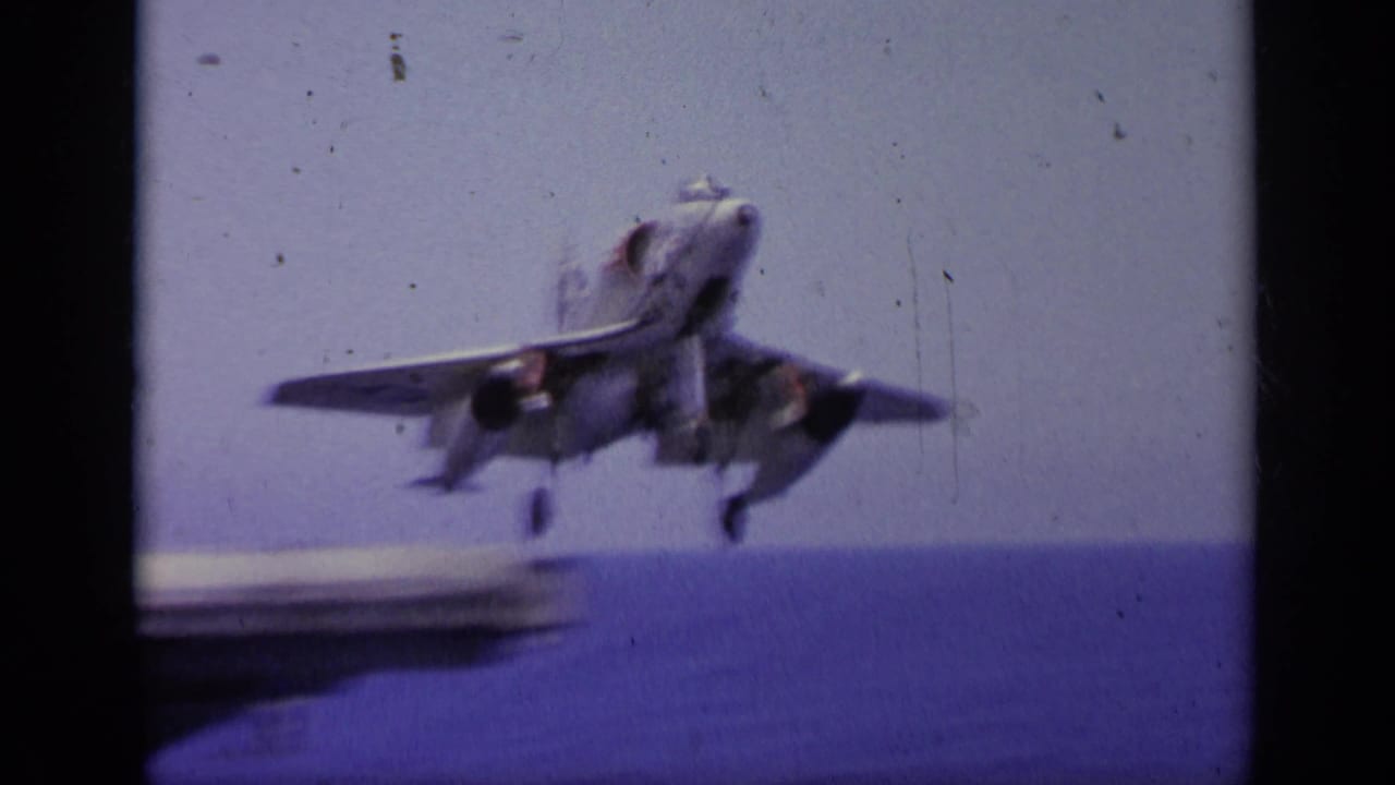 Jet aircraft airborne beyond the edge of an aircraft carrier deck.