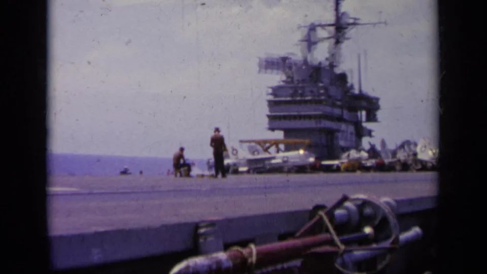 1963 Greece 8mm frame showing carrier flight deck activity, crew figures, aircraft, and the ship island structure.