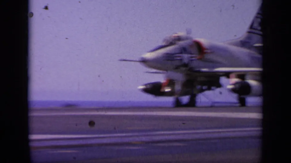 A military jet moves along the aircraft carrier deck in soft, motion-blurred 8mm footage from Greece in 1963.