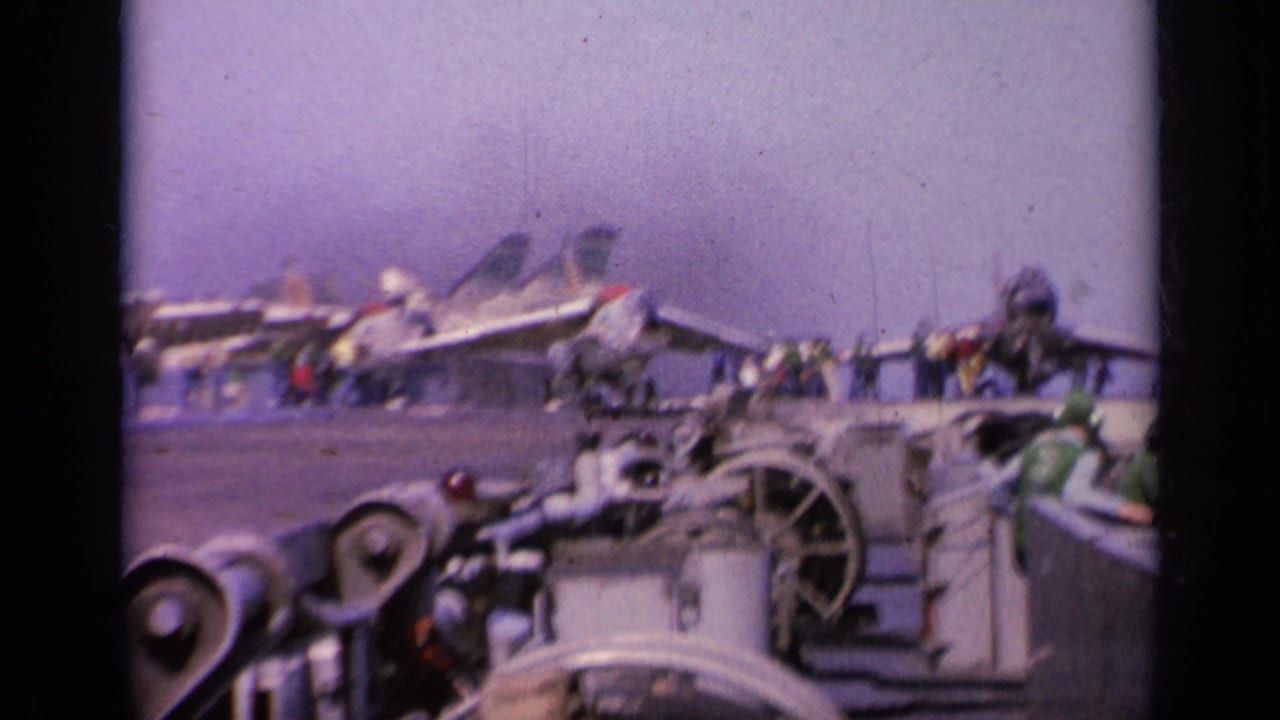 1963 Greece 8mm view of an aircraft carrier deck with military jets parked in a row, crew figures, deck machinery, and the sea beyond.