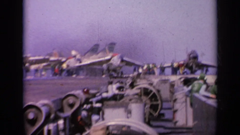 1963 Greece 8mm view of an aircraft carrier deck with military jets parked in a row, crew figures, deck machinery, and the sea beyond.