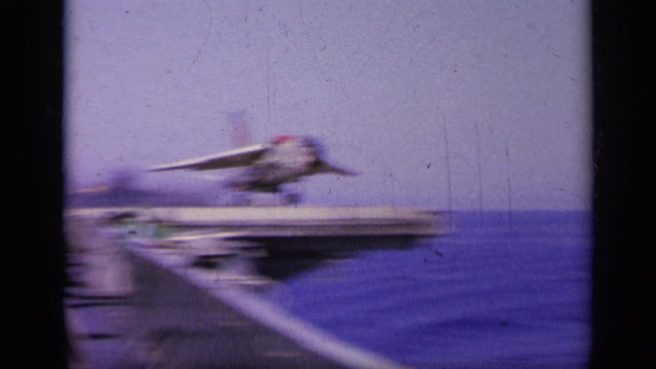 Military jet launching from an aircraft carrier over open water.