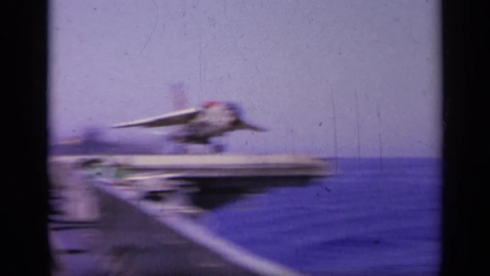 A military jet lifts from the carrier deck over the sea, captured with motion blur and 8mm color shifts during the launch.