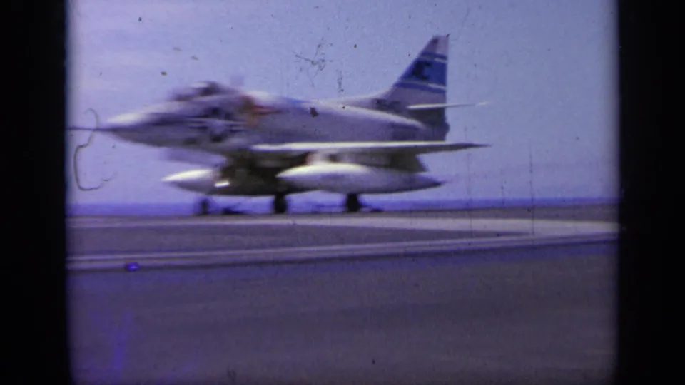 1963 Greece 8mm frame showing a carrier-based jet moving quickly along the flight deck, with open sea behind it.