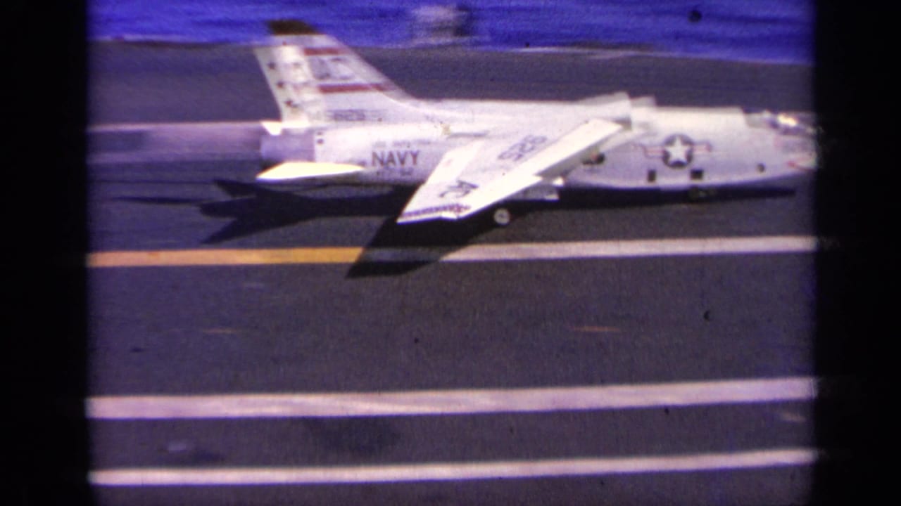 1963 Greece footage shows a white U.S. Navy jet marked AC on an aircraft carrier deck beside open water.