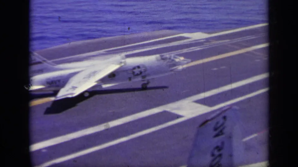 1963 Greece metadata supports this 8mm view of a white naval jet on a carrier deck with runway markings and sea in the background.