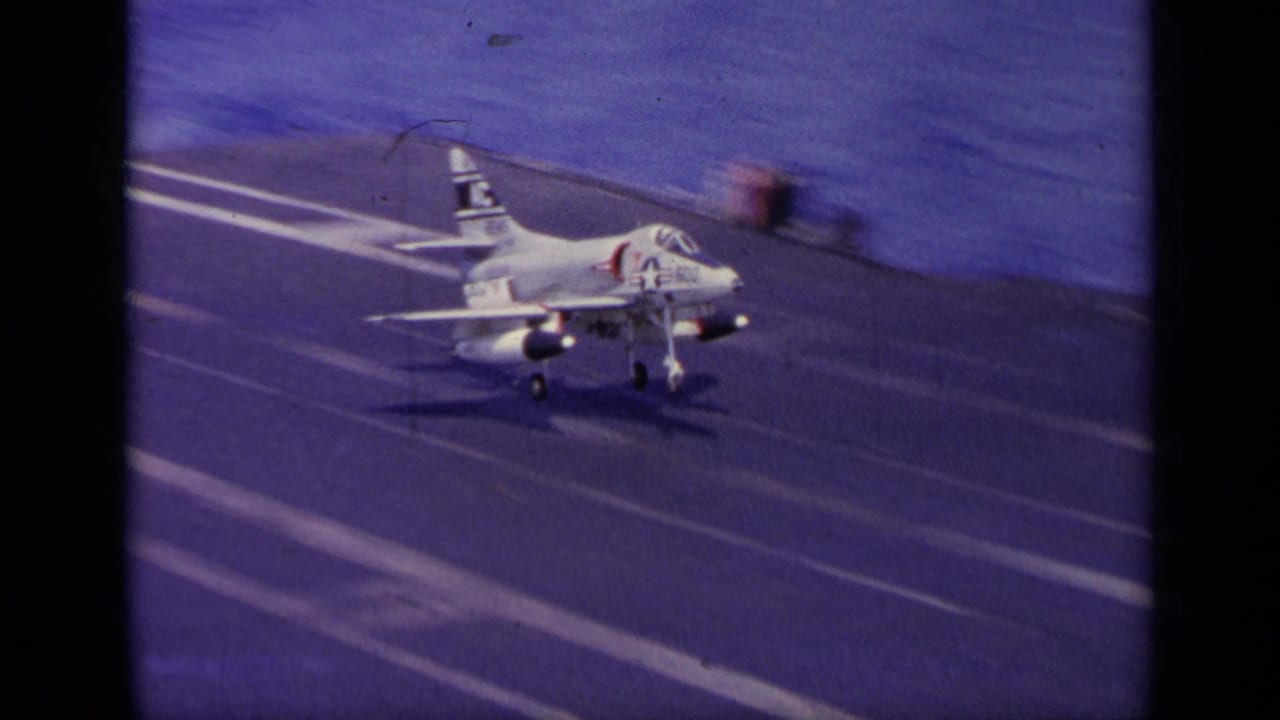 1963 8mm frame from Greece showing a U.S. Navy jet approaching or touching down on an aircraft carrier deck at sea.