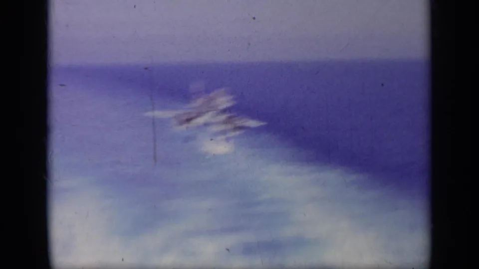 Soft, motion-blurred 1963 8mm frame from the carrier sequence, with a faint aircraft shape against sea and deck tones.
